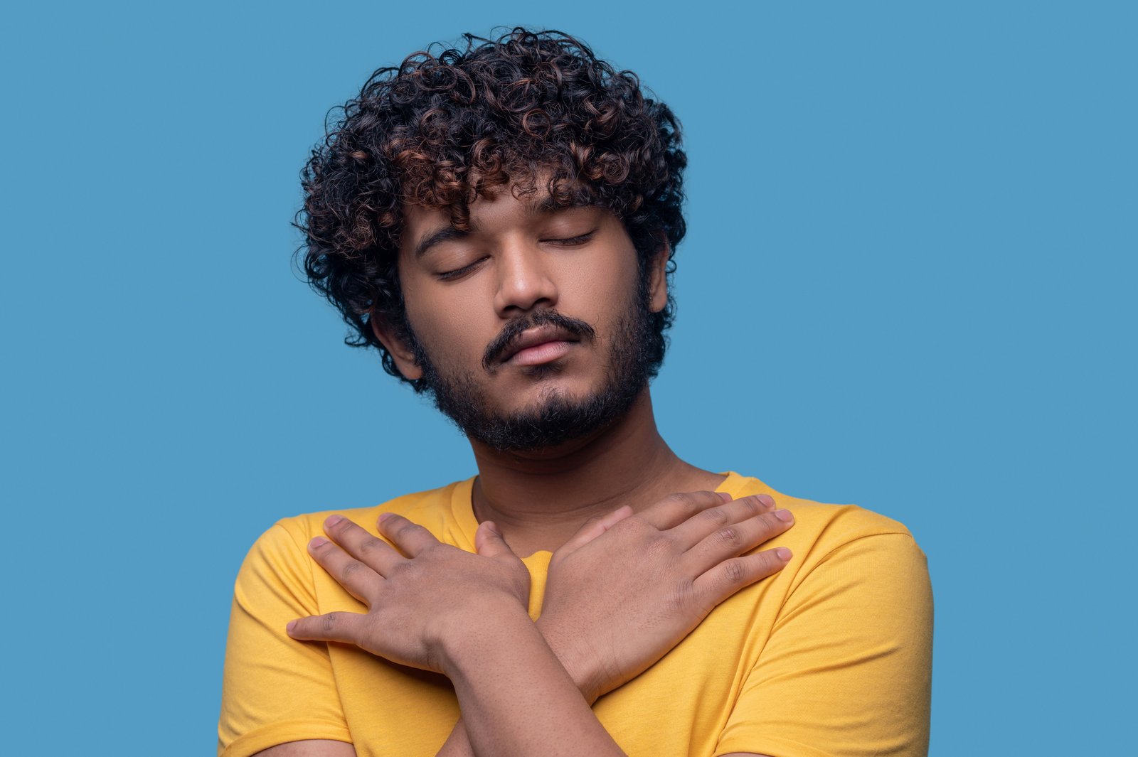Salud mental masculina. retrato de un joven sereno con los ojos cerrados de pie contra el fondo azul